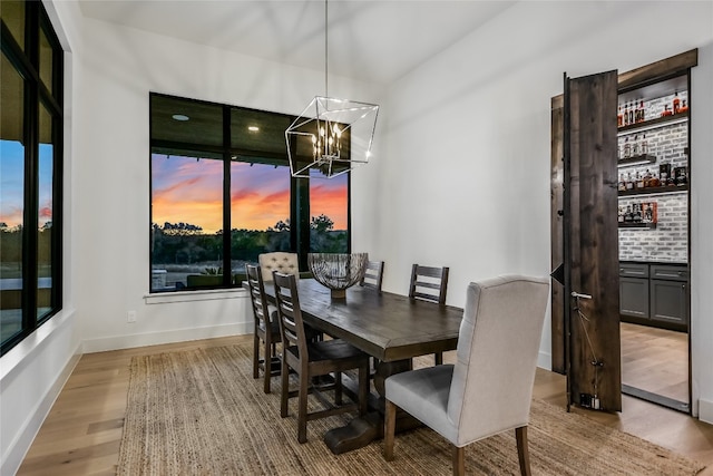 dining area featuring a notable chandelier, baseboards, light wood-style floors, and a dry bar