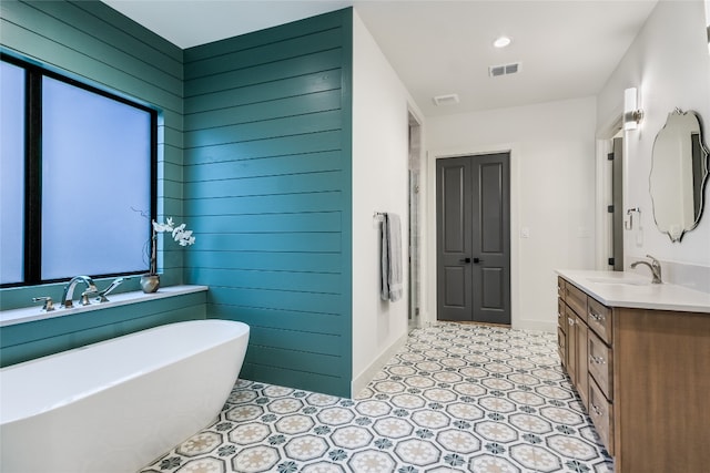 bathroom with visible vents, wooden walls, baseboards, a freestanding bath, and vanity