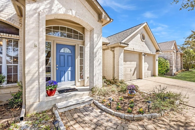 view of exterior entry featuring concrete driveway, a garage, brick siding, and a shingled roof