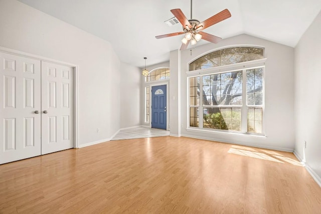 unfurnished living room featuring a wealth of natural light, light wood-type flooring, ceiling fan with notable chandelier, and vaulted ceiling