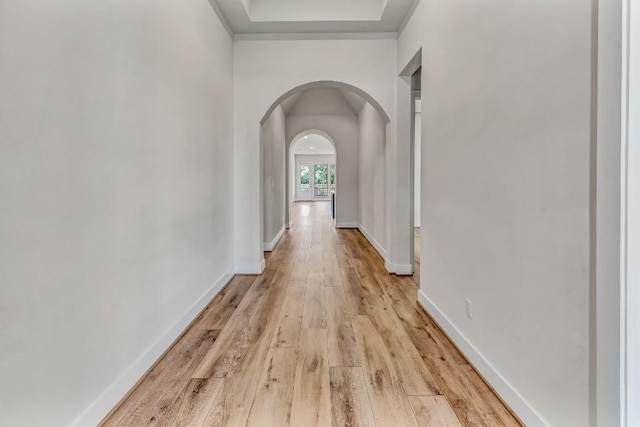 corridor featuring baseboards, arched walkways, and light wood-style flooring