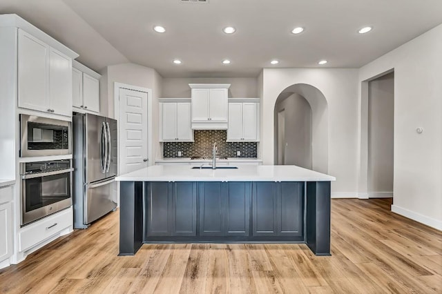 kitchen featuring an island with sink, a sink, decorative backsplash, light countertops, and stainless steel appliances