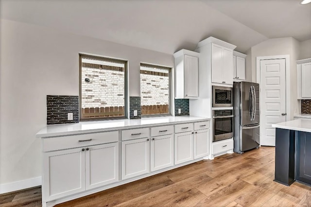 kitchen featuring light wood-type flooring, tasteful backsplash, appliances with stainless steel finishes, white cabinets, and light countertops