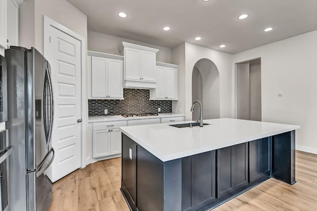 kitchen featuring stovetop, a kitchen island with sink, freestanding refrigerator, a sink, and light wood-style floors