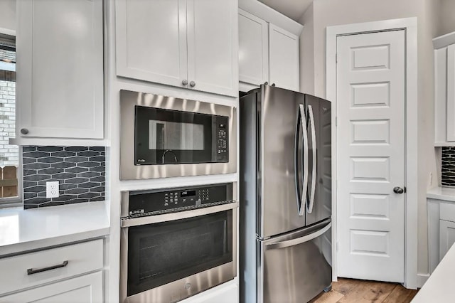 kitchen with tasteful backsplash, white cabinets, stainless steel appliances, and light countertops