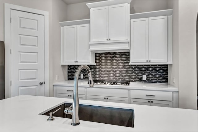 kitchen featuring premium range hood, stainless steel gas cooktop, light countertops, decorative backsplash, and a sink