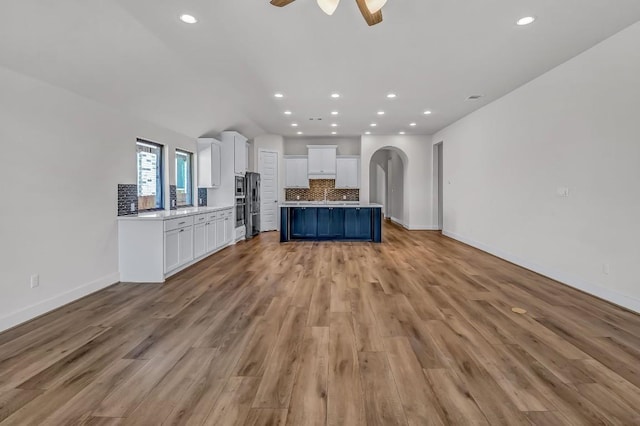 kitchen featuring arched walkways, decorative backsplash, light countertops, white cabinets, and light wood-style floors