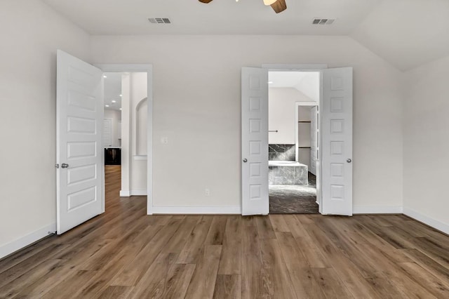 unfurnished bedroom featuring vaulted ceiling, wood finished floors, and visible vents