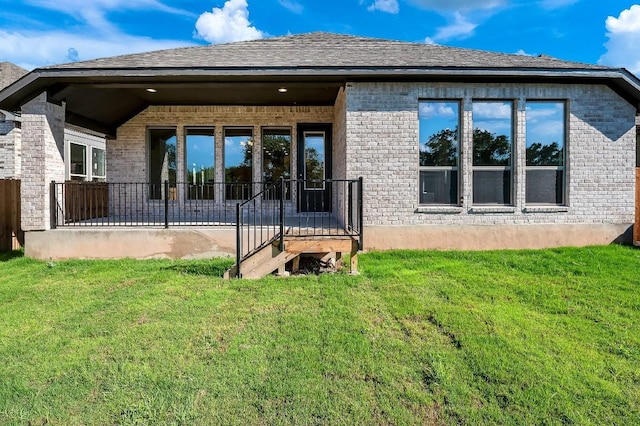 back of house with brick siding, a lawn, and a shingled roof