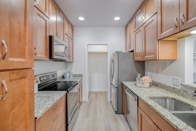 kitchen with light wood-type flooring, a sink, light stone counters, recessed lighting, and stainless steel appliances