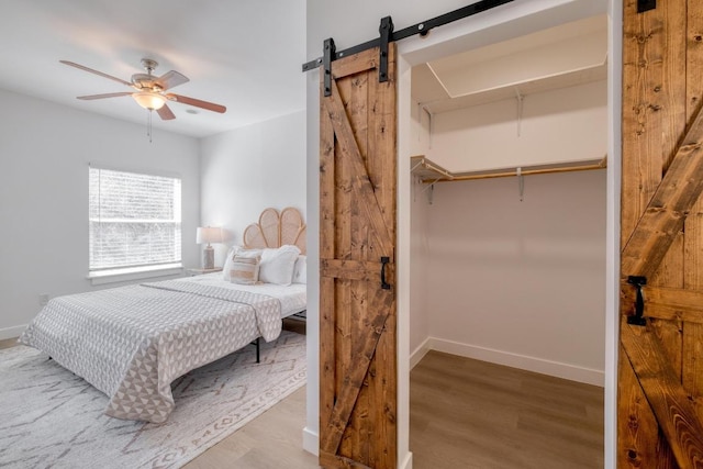 bedroom with a barn door, baseboards, wood finished floors, and a ceiling fan