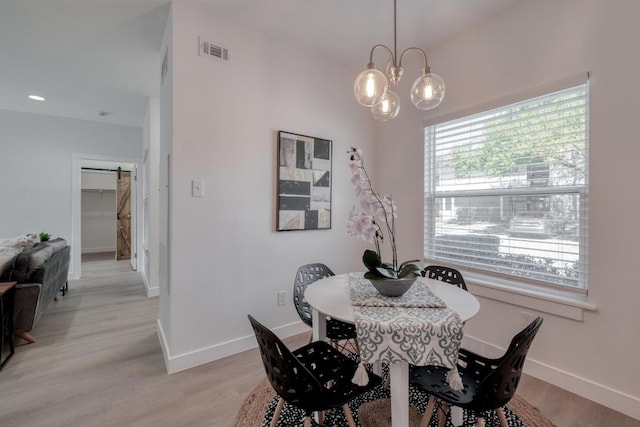 dining room with a barn door, baseboards, visible vents, and light wood finished floors