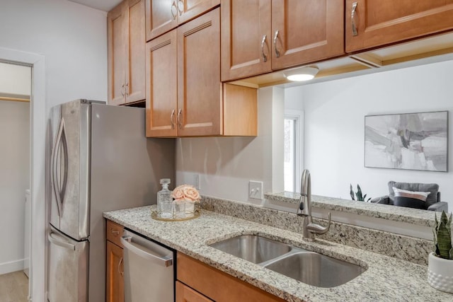 kitchen with a sink, light stone countertops, stainless steel dishwasher, and brown cabinetry