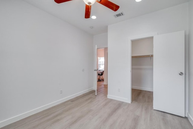 unfurnished bedroom featuring baseboards, visible vents, a closet, a walk in closet, and light wood-type flooring