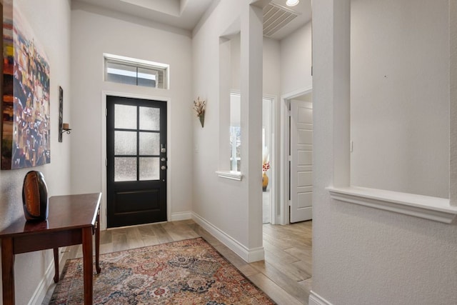 entrance foyer with visible vents, baseboards, wood finished floors, and a towering ceiling