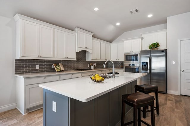 kitchen with a kitchen bar, decorative backsplash, visible vents, and appliances with stainless steel finishes