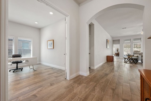 hall with light wood-style flooring, baseboards, and arched walkways