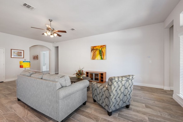 living room with visible vents, arched walkways, baseboards, and a ceiling fan