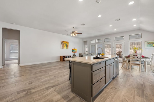 kitchen featuring light wood finished floors, a sink, gray cabinetry, light countertops, and stainless steel dishwasher