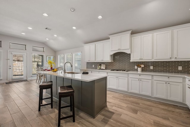 kitchen featuring visible vents, a breakfast bar, light countertops, decorative backsplash, and a sink