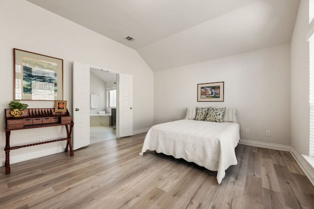 bedroom with vaulted ceiling, wood finished floors, baseboards, and connected bathroom