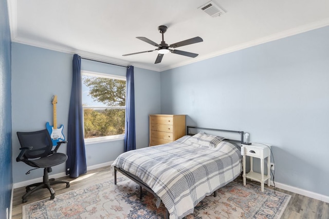 bedroom with visible vents, baseboards, wood finished floors, and ornamental molding