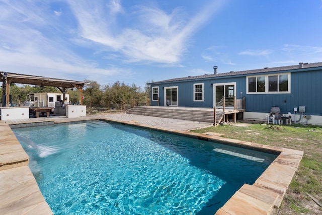 back of property featuring a deck, an outdoor pool, and an outdoor kitchen