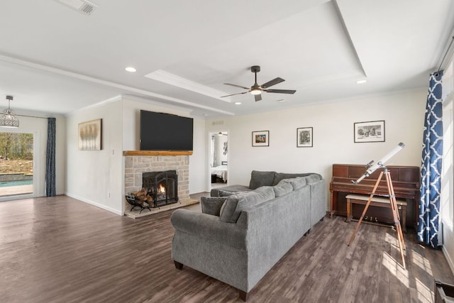 living area featuring a brick fireplace, a tray ceiling, ornamental molding, dark wood-style floors, and a ceiling fan