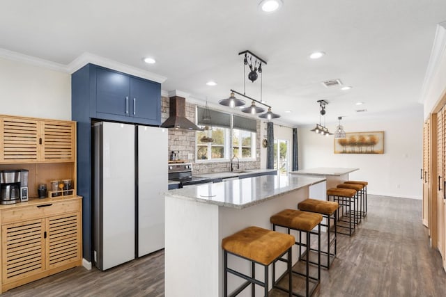 kitchen with visible vents, a kitchen island, wall chimney range hood, stainless steel range with electric stovetop, and freestanding refrigerator