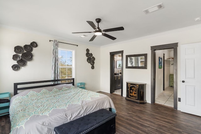 bedroom featuring wood finished floors, visible vents, baseboards, crown molding, and connected bathroom