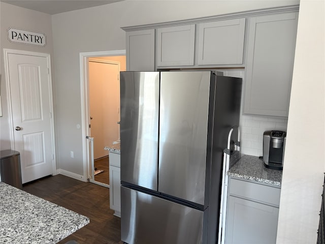 kitchen with light stone counters, dark wood-style floors, freestanding refrigerator, gray cabinetry, and decorative backsplash