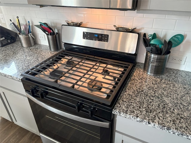 interior details featuring gas stove, light stone counters, backsplash, and dark wood finished floors