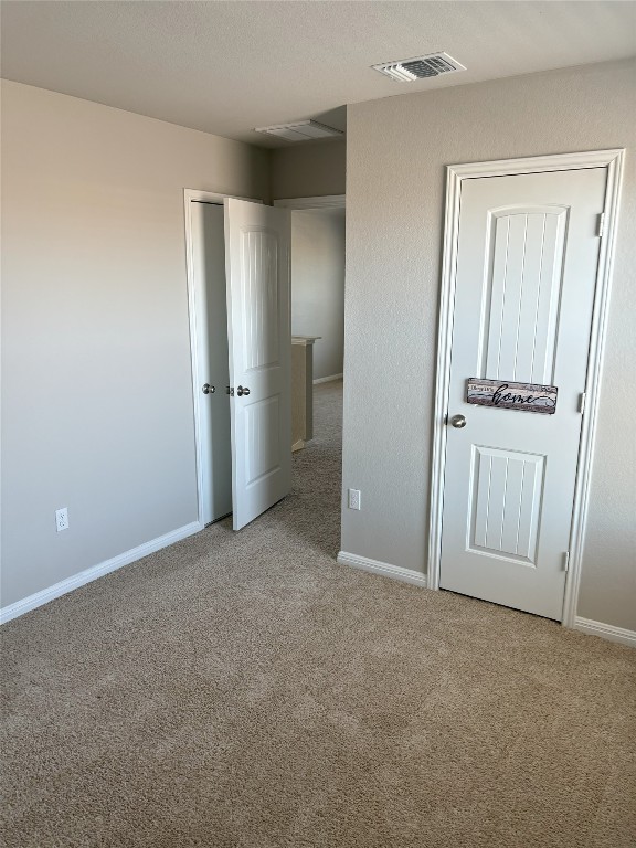 unfurnished bedroom featuring visible vents, a textured ceiling, baseboards, and carpet