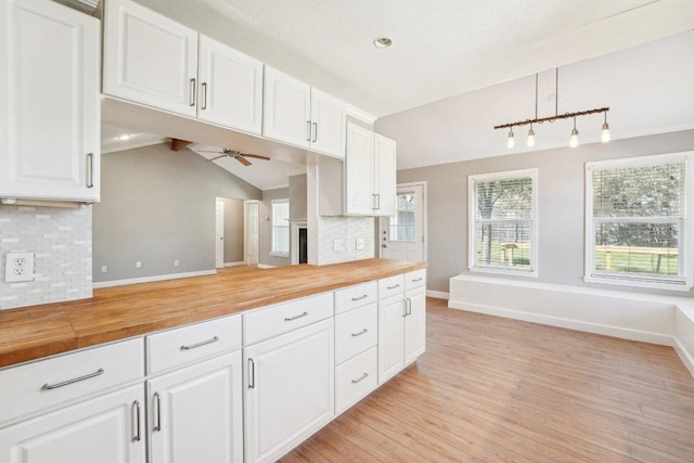 kitchen with tasteful backsplash, butcher block counters, light wood-type flooring, and vaulted ceiling