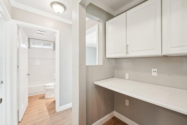 interior space with baseboards, light wood-style floors, ornamental molding, and built in desk