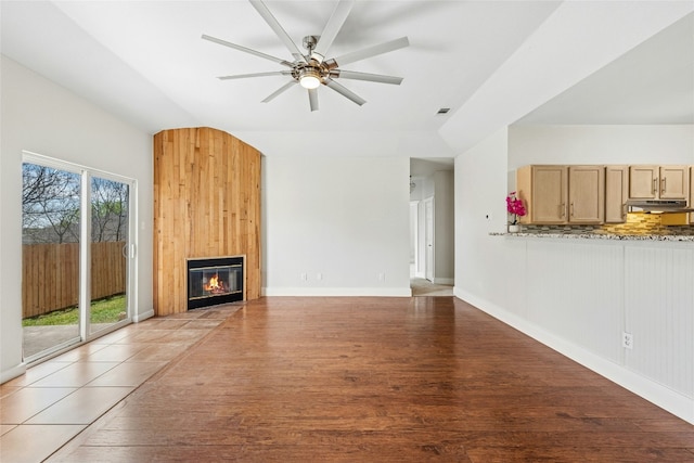 unfurnished living room featuring vaulted ceiling, light wood-style flooring, a ceiling fan, and a large fireplace