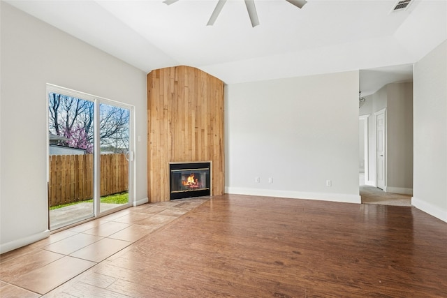 unfurnished living room with visible vents, a ceiling fan, wood finished floors, a fireplace, and vaulted ceiling