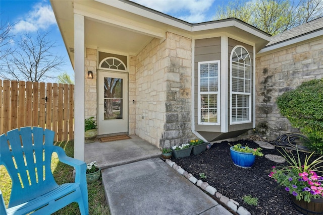 view of exterior entry featuring fence and stone siding