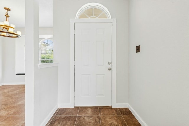 foyer featuring baseboards, an inviting chandelier, and dark tile patterned floors