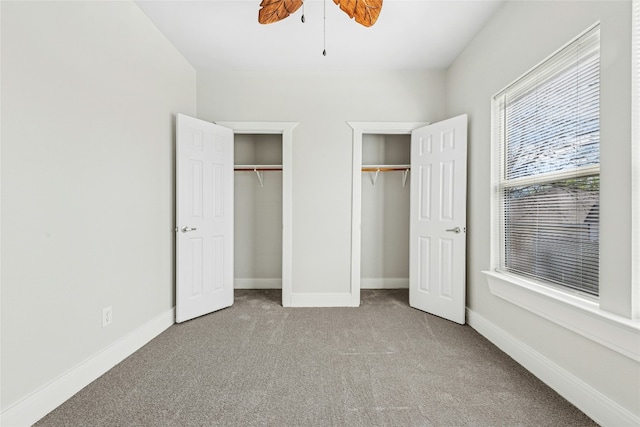 unfurnished bedroom with baseboards, ceiling fan, two closets, and carpet