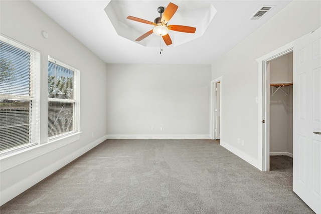 unfurnished bedroom featuring a tray ceiling, visible vents, a walk in closet, and carpet flooring