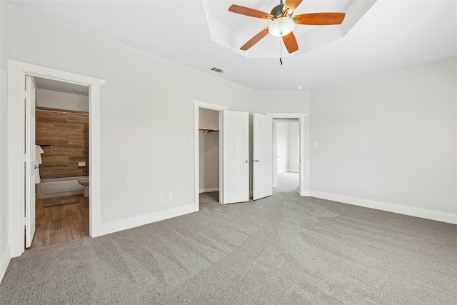 unfurnished bedroom featuring a raised ceiling, a spacious closet, visible vents, and carpet floors