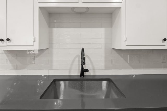 kitchen with a sink, decorative backsplash, dark countertops, and white cabinetry