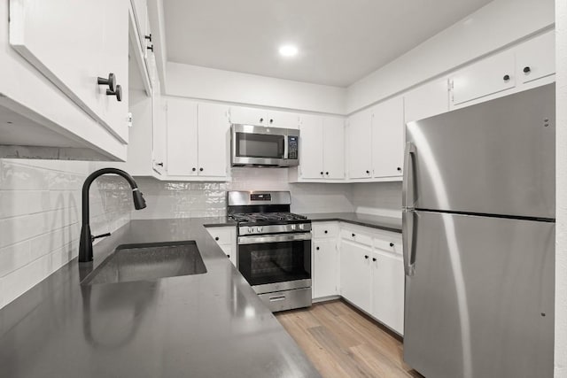 kitchen featuring a sink, decorative backsplash, stainless steel appliances, light wood-style floors, and white cabinetry