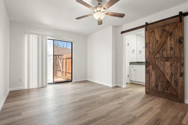 unfurnished room with a barn door, baseboards, light wood-type flooring, and ceiling fan