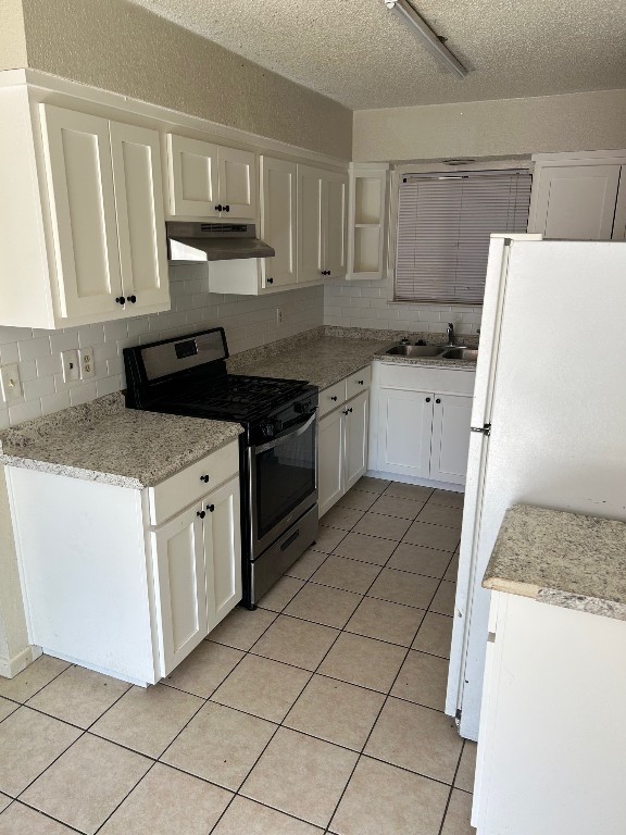 kitchen featuring light tile patterned floors, stainless steel range with gas stovetop, freestanding refrigerator, white cabinets, and under cabinet range hood