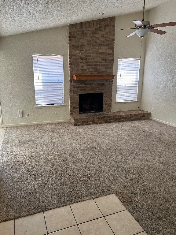 unfurnished living room featuring a brick fireplace, light colored carpet, vaulted ceiling, light tile patterned floors, and a textured ceiling