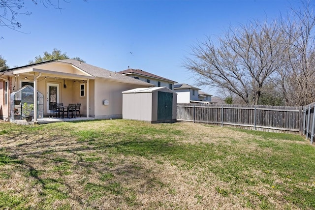 back of property with an outbuilding, a patio, a shed, a fenced backyard, and a lawn