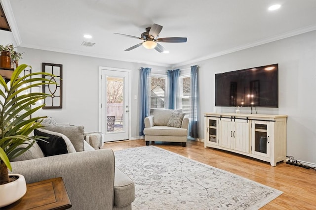 living area with baseboards, visible vents, light wood-style flooring, ceiling fan, and crown molding