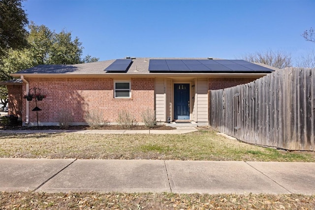 view of front of property with brick siding, solar panels, a front yard, and fence